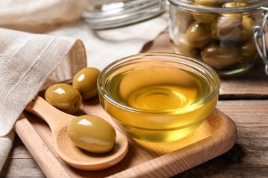 Photo of Bowl of cooking oil and olives on wooden table, closeup