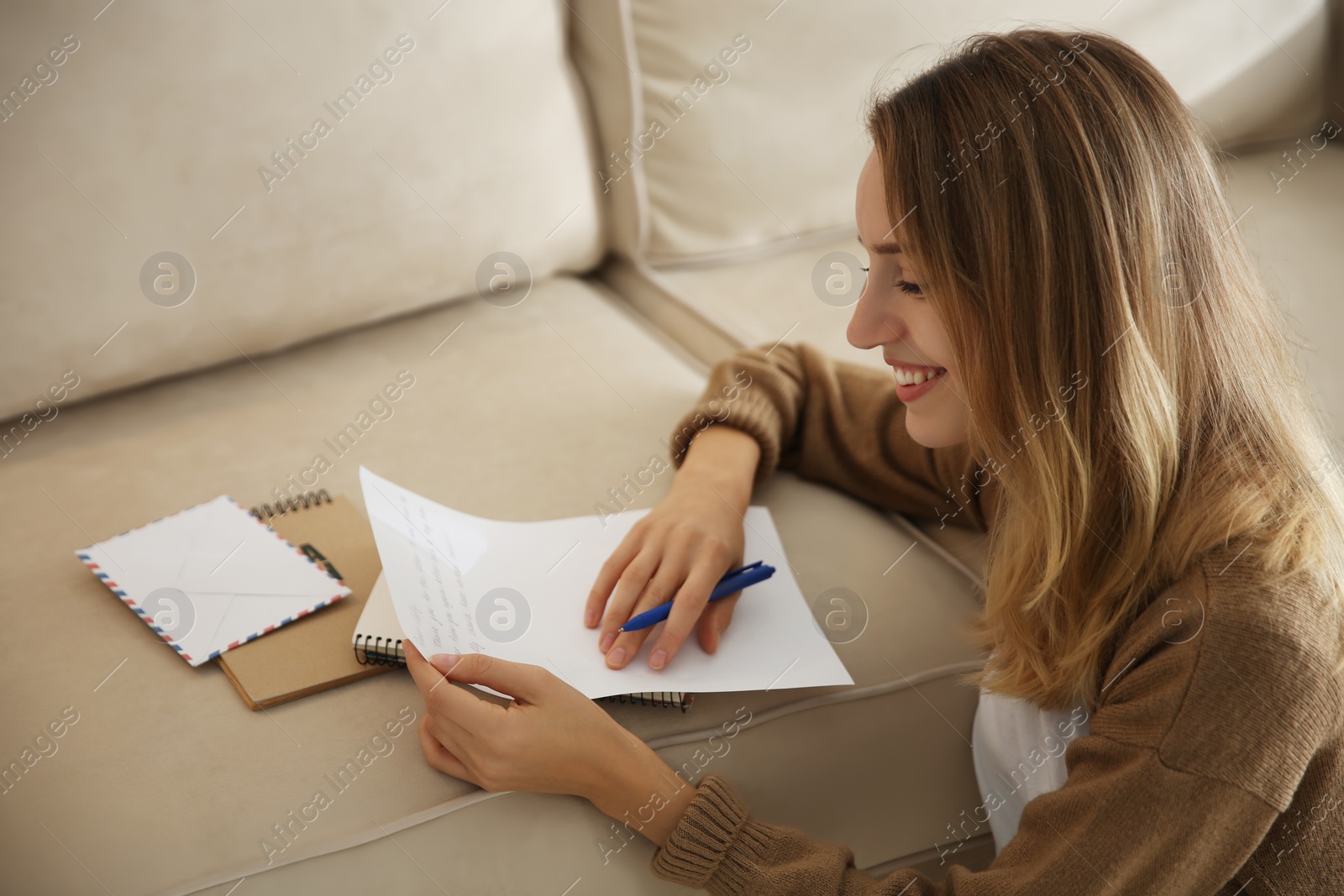 Photo of Happy woman writing letter on sofa at home