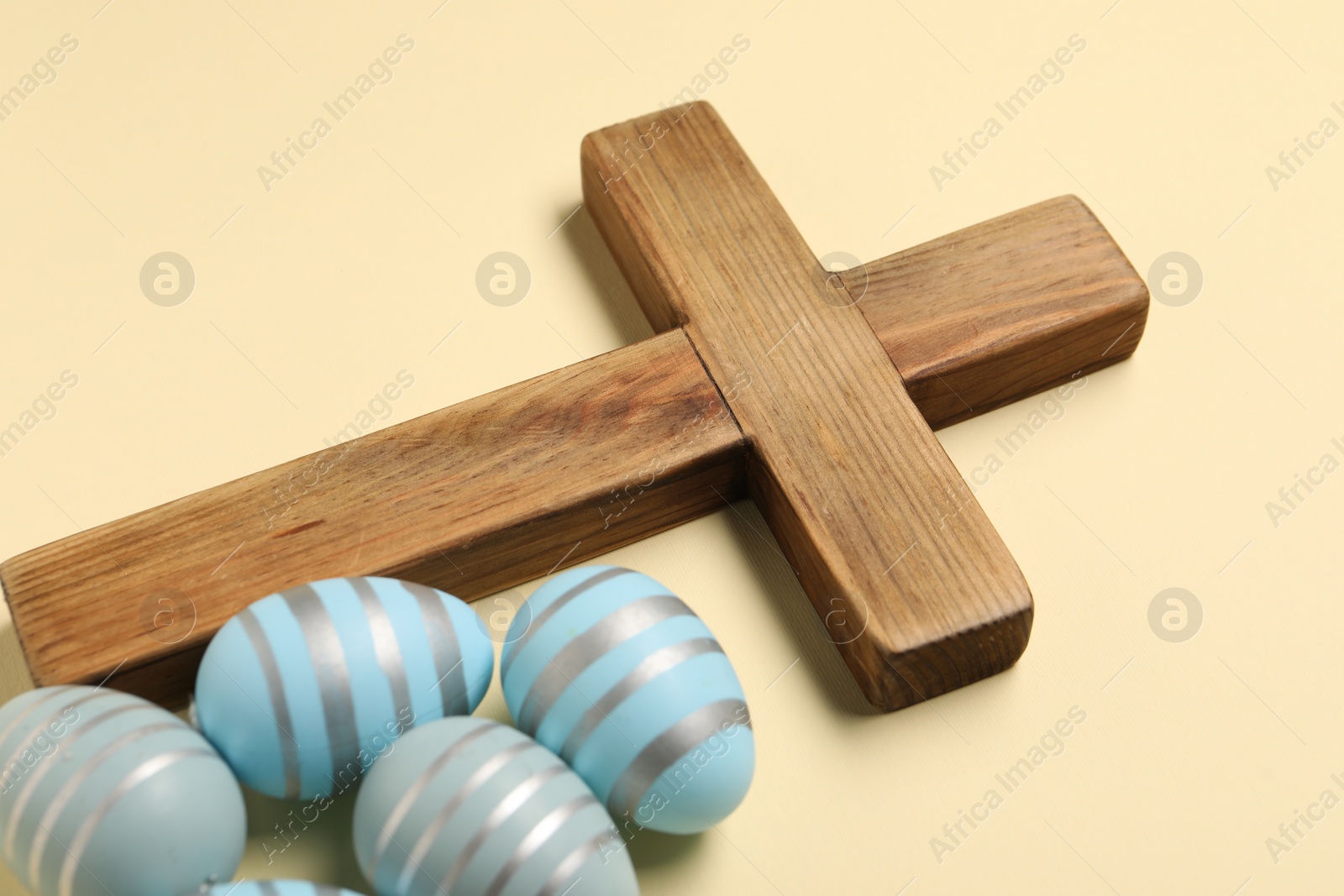 Photo of Wooden cross and painted Easter eggs on beige background