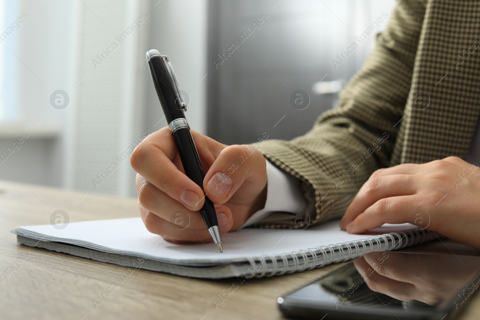 Photo of Woman writing in notebook at wooden table indoors, closeup