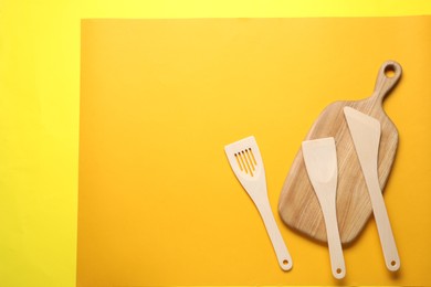 Photo of Different wooden spatulas and board on color background, flat lay. Space for text