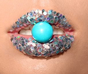 Beautiful young model with extravagant makeup holding candy in lips, closeup