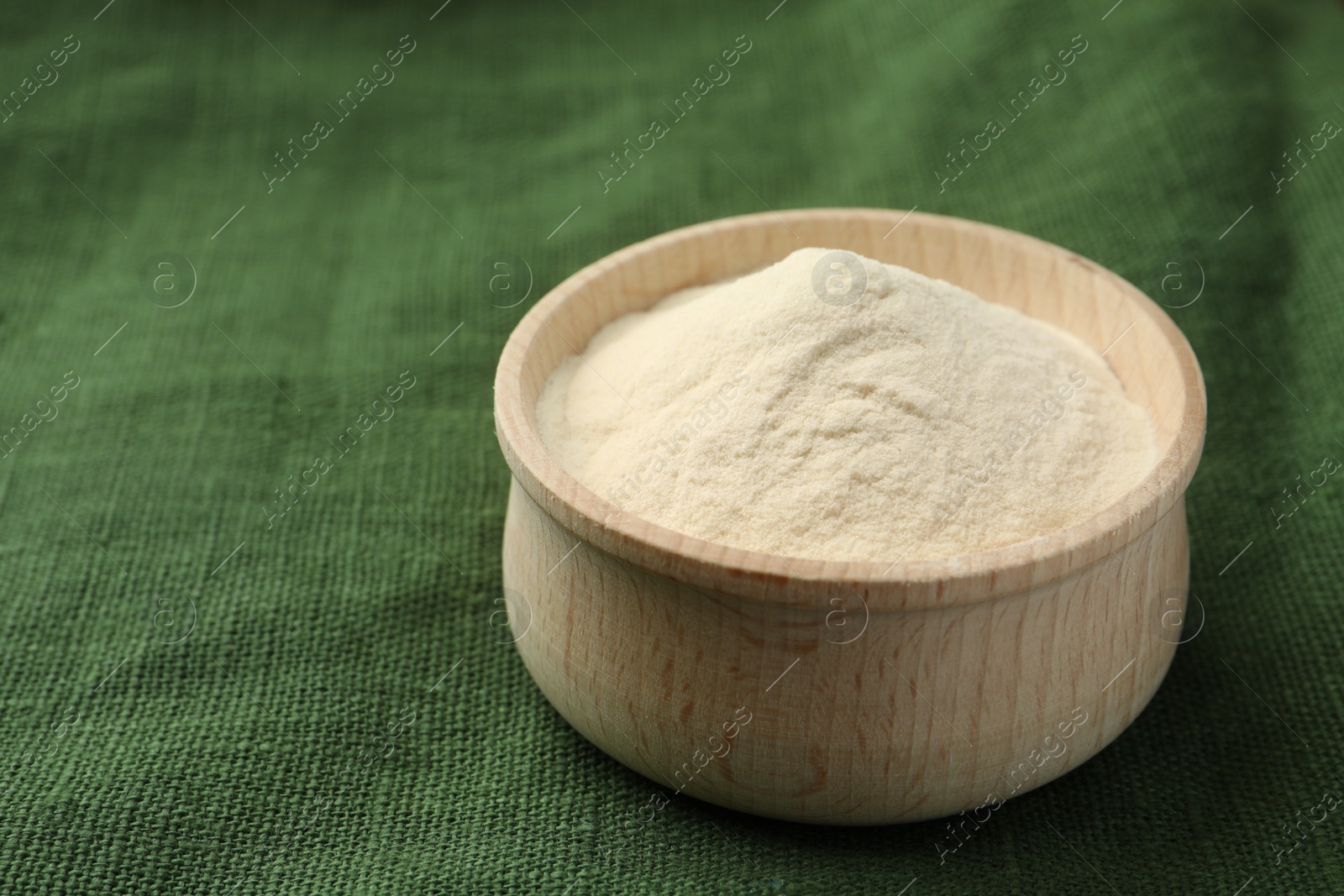 Photo of Wooden bowl of agar-agar powder on green tablecloth, closeup. Space for text