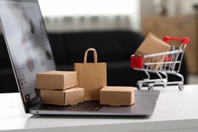 Photo of Online store. Laptop, small parcels and shopping bag on white table