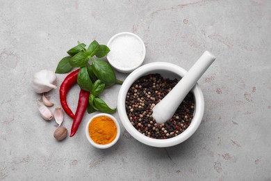 Photo of Mortar with pestle and different spices on light grey table, flat lay