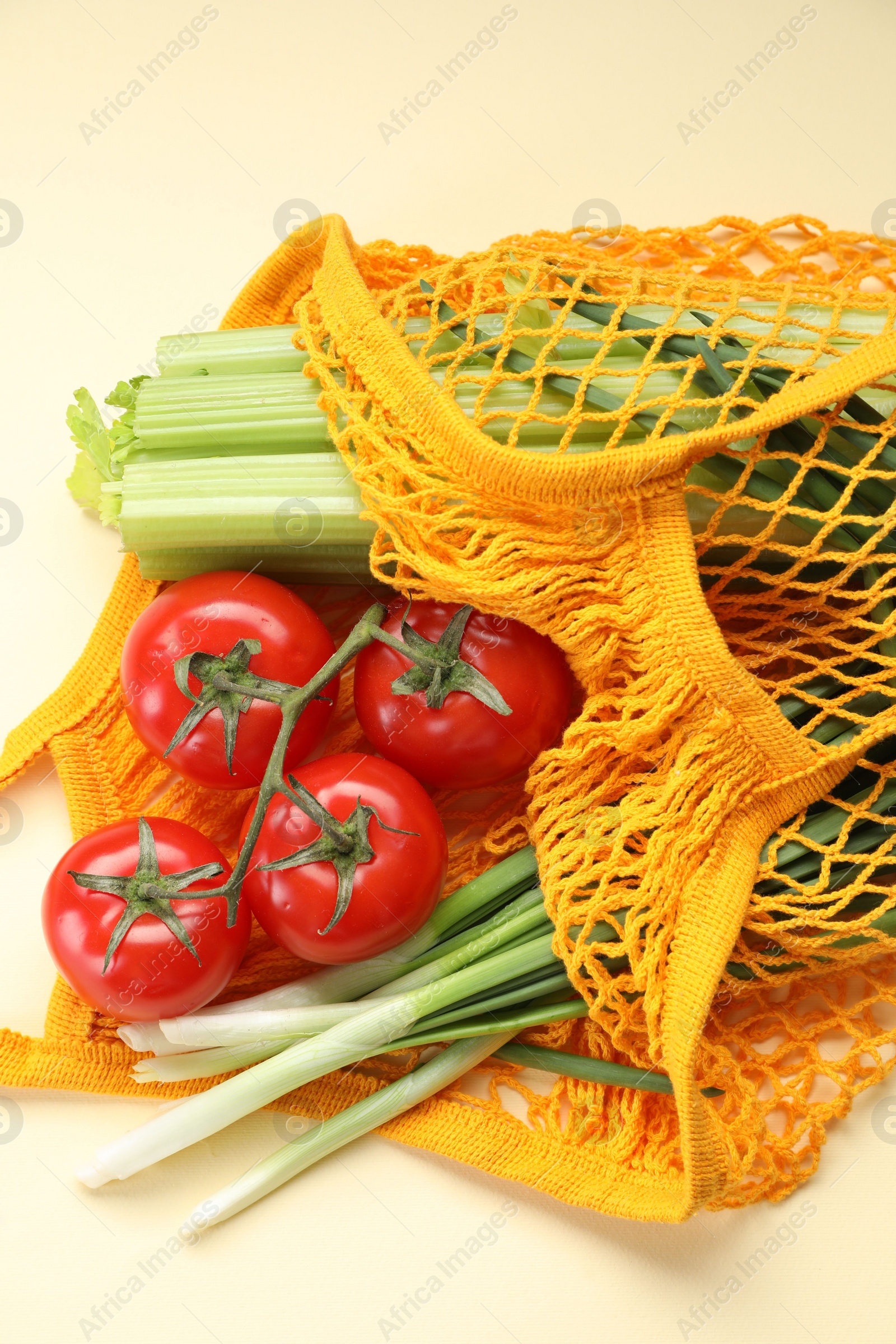 Photo of String bag with different vegetables on beige background, closeup