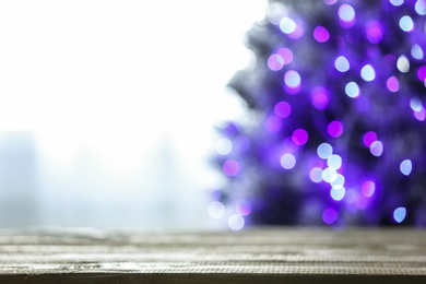 Photo of Blurred view of beautiful Christmas tree with purple lights near window indoors, focus on wooden table. Space for text