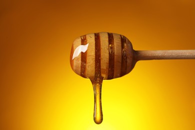 Photo of Pouring honey from dipper against golden background, closeup