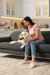 Happy woman with cute Labrador Retriever dog on sofa at home. Adorable pet