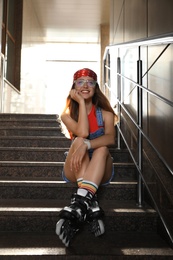 Photo of Beautiful young woman with roller skates sitting on stairs outdoors