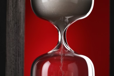 Photo of Hourglass with flowing sand on red background, closeup