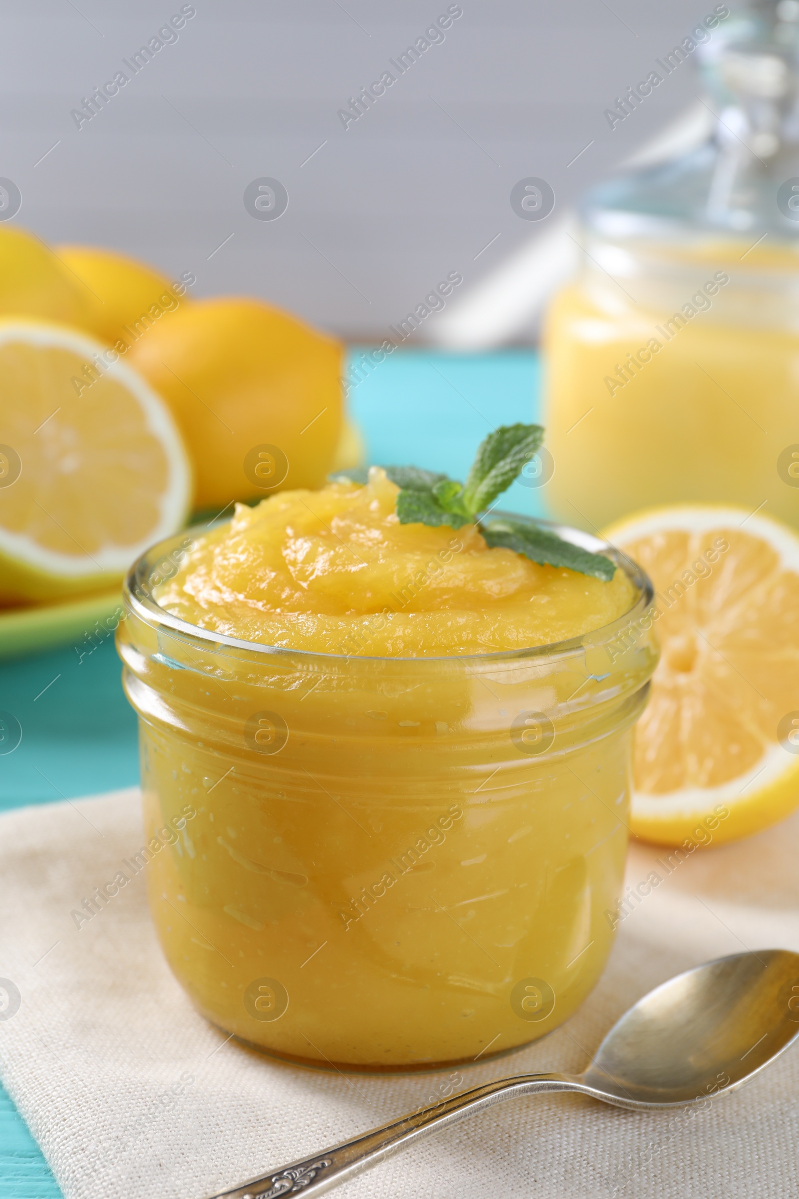 Photo of Delicious lemon curd in glass jar, fresh citrus fruits, mint and spoon on table
