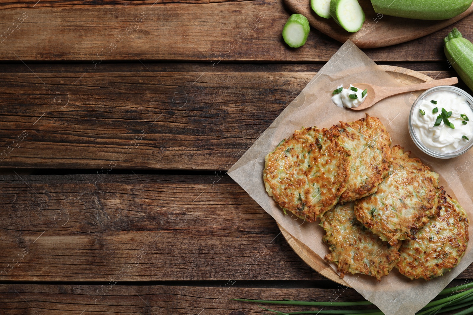 Photo of Delicious zucchini fritters with sour cream served on wooden table, flat lay. Space for text