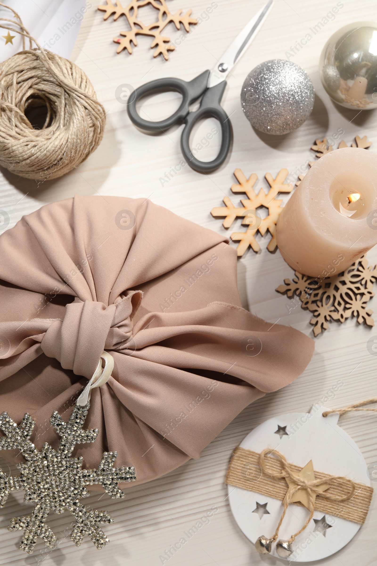 Photo of Furoshiki technique. Flat lay composition with gift packed in pink fabric and decorative snowflakes on white wooden table