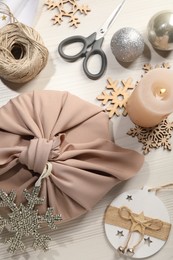 Photo of Furoshiki technique. Flat lay composition with gift packed in pink fabric and decorative snowflakes on white wooden table