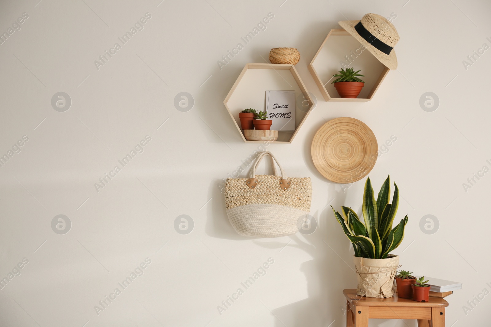 Photo of Hexagon wooden shelves with beautiful plants and accessories on light wall. Space for text