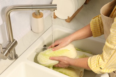 Photo of Woman washing fresh chinese cabbage under tap water in kitchen sink, closeup