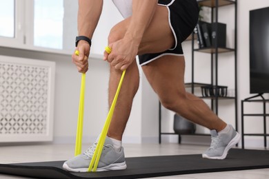 Athletic man doing exercise with elastic resistance band on mat at home, closeup