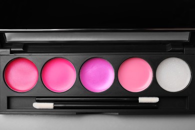 Photo of Cream lipstick palette with brushes on grey table, top view. Professional cosmetic product