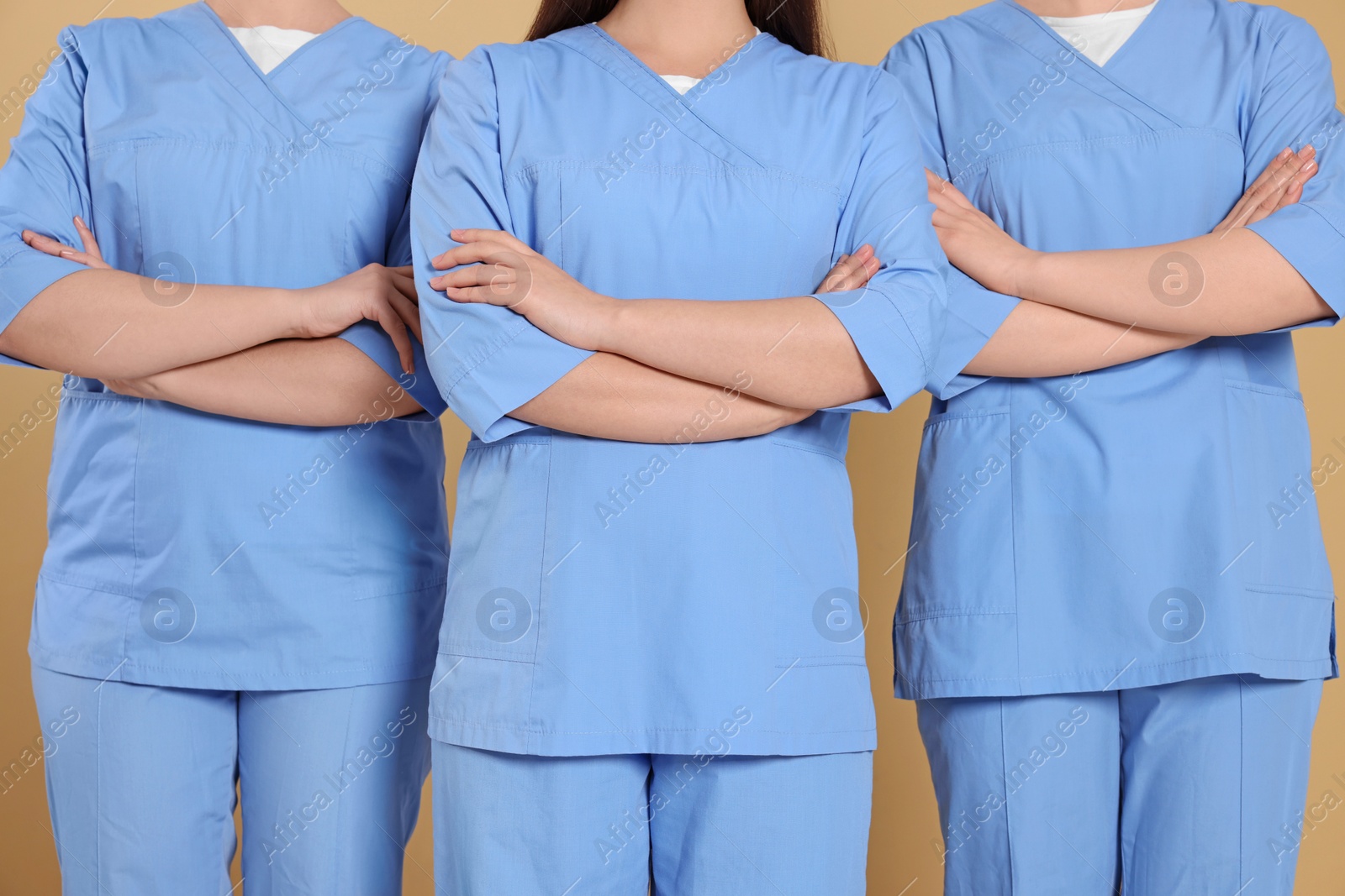 Photo of Nurses in medical uniforms on light brown background, closeup