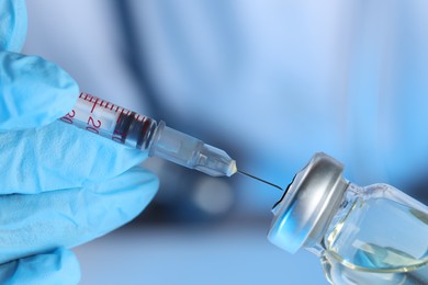 Photo of Doctor inserting syringe into glass vial with medication, closeup