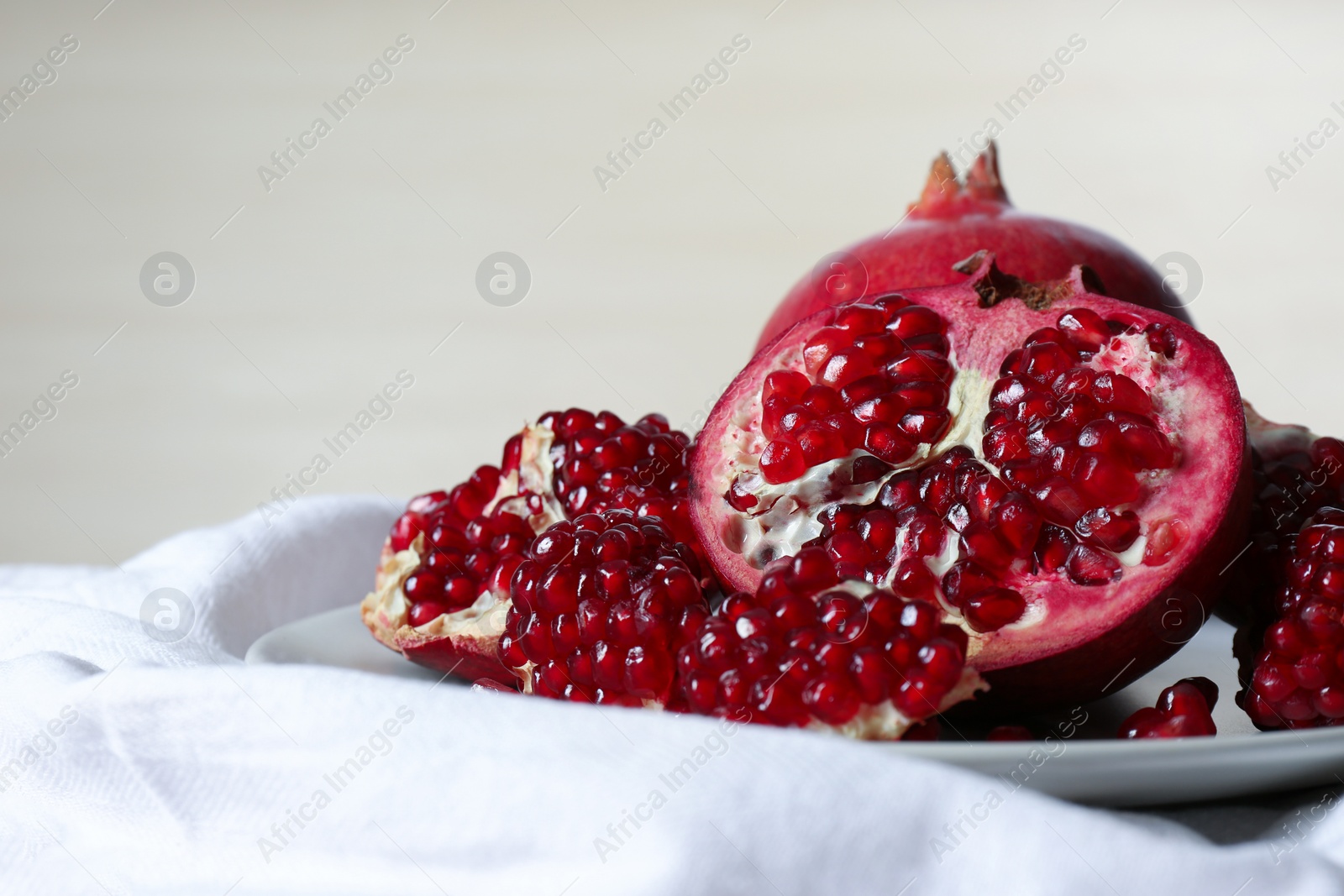 Photo of Plate with ripe pomegranates on table against light background, space for text