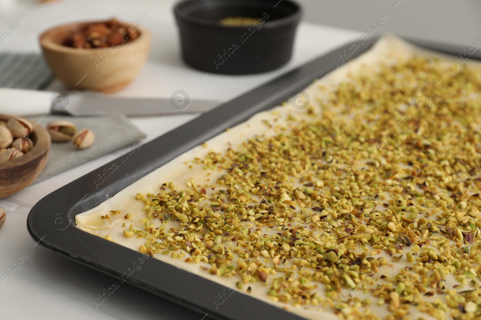 Photo of Making delicious baklava. Baking pan with dough and chopped nut mix on white table, closeup