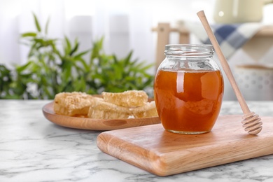 Photo of Glass jar with sweet honey and dipper on wooden board