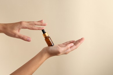 Woman with bottle of cosmetic serum on beige background, closeup. Space for text