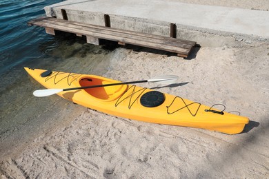 Photo of Yellow kayak with paddle on beach near river. Summer camp activity