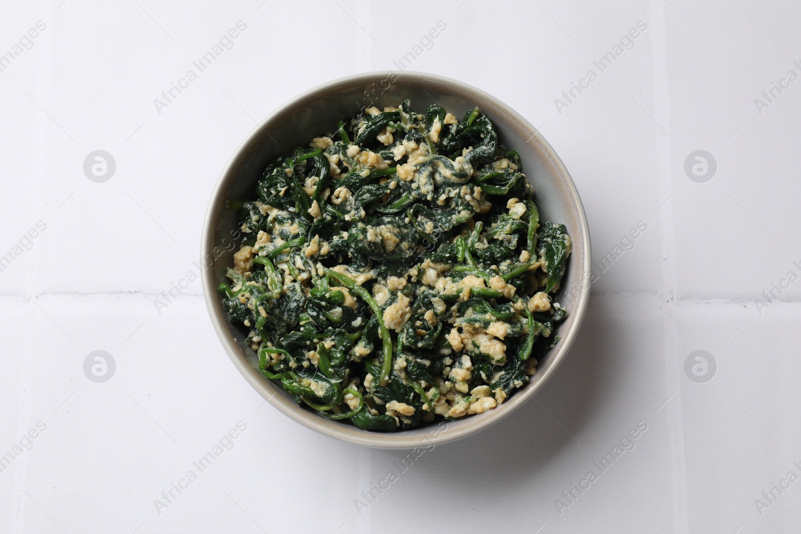 Photo of Tasty spinach dip with egg in bowl on white tiled table, top view