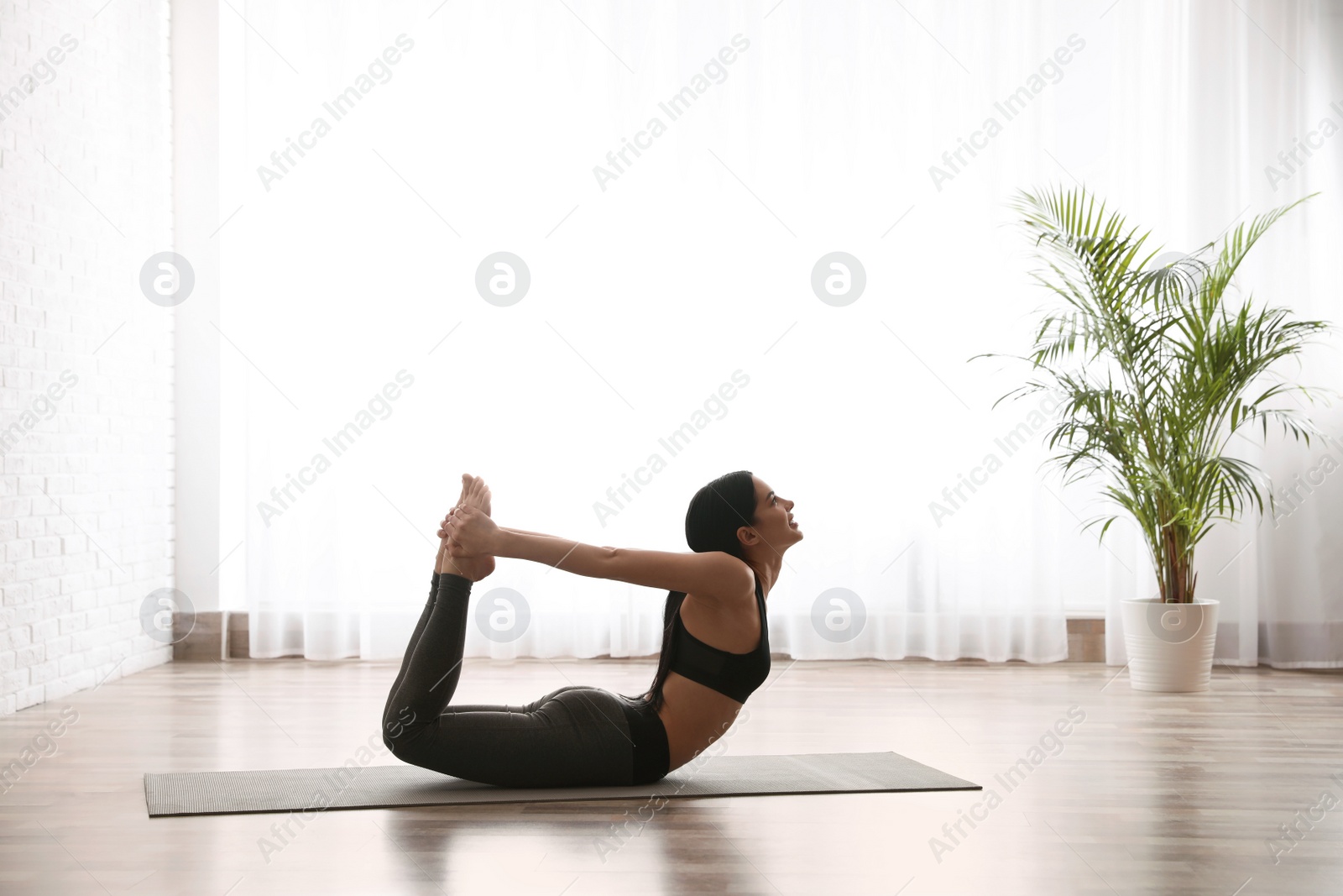 Photo of Young woman practicing bow asana in yoga studio. Dhanurasana pose