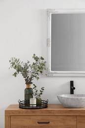 Photo of Beautiful eucalyptus branches near vessel sink on bathroom vanity. Interior design