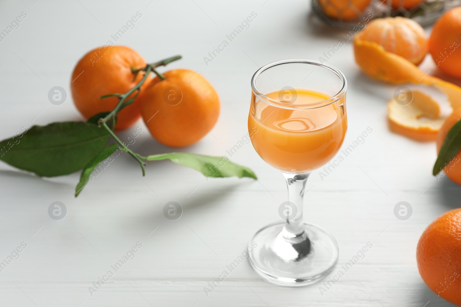 Photo of Tasty tangerine liqueur in glass and fresh fruits on white wooden table