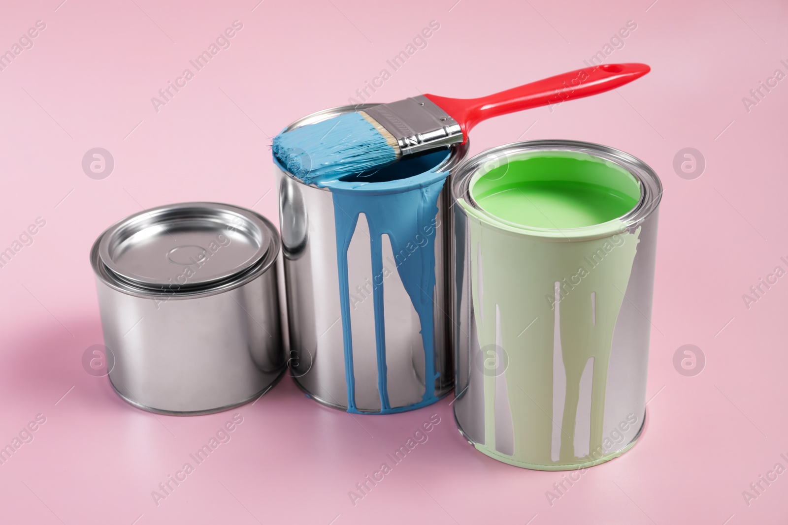 Photo of Cans of paints and brush on pink background