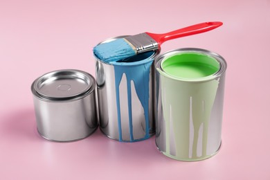 Photo of Cans of paints and brush on pink background