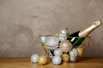 Christmas balls with bottle of champagne in decorative basket and space for text on gray background