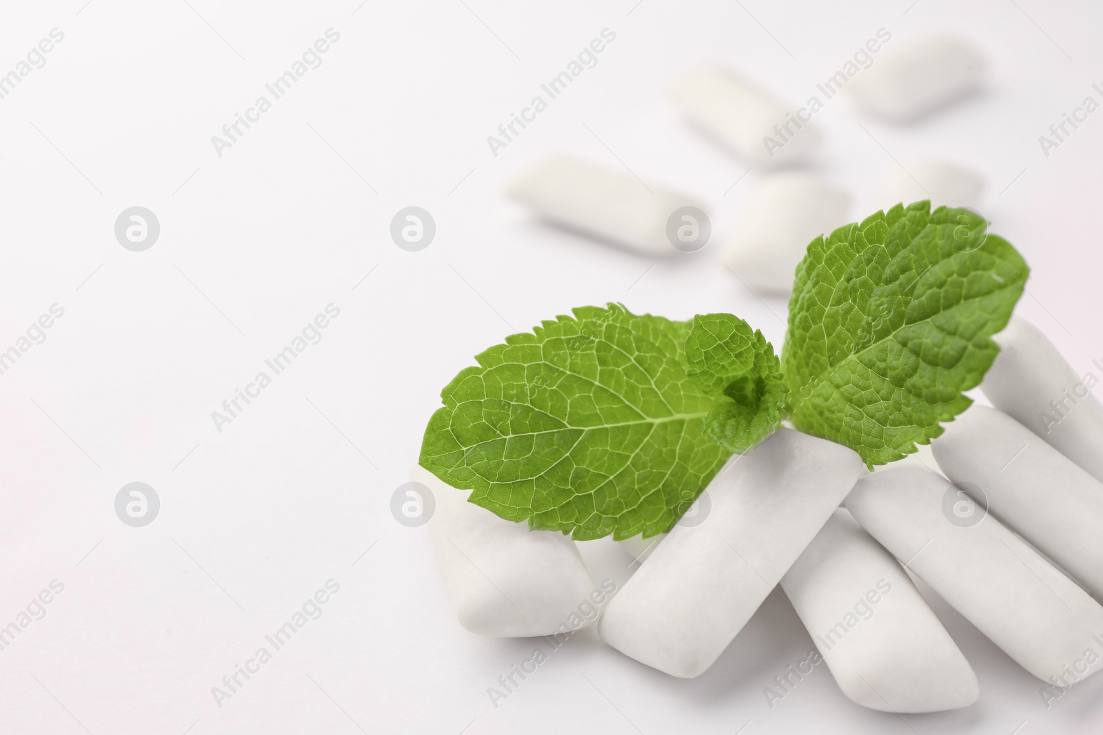 Photo of Tasty chewing gums and mint leaves on white background, closeup. Space for text