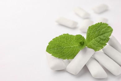 Tasty chewing gums and mint leaves on white background, closeup. Space for text