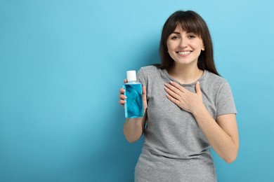 Young woman with mouthwash on light blue background, space for text