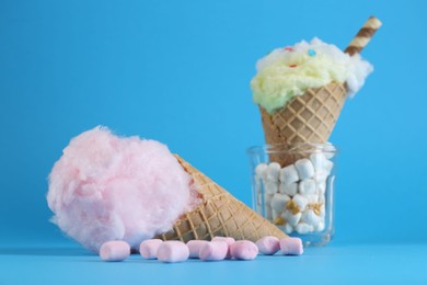 Photo of Sweet cotton candy in waffle cone and marshmallows on light blue background, closeup