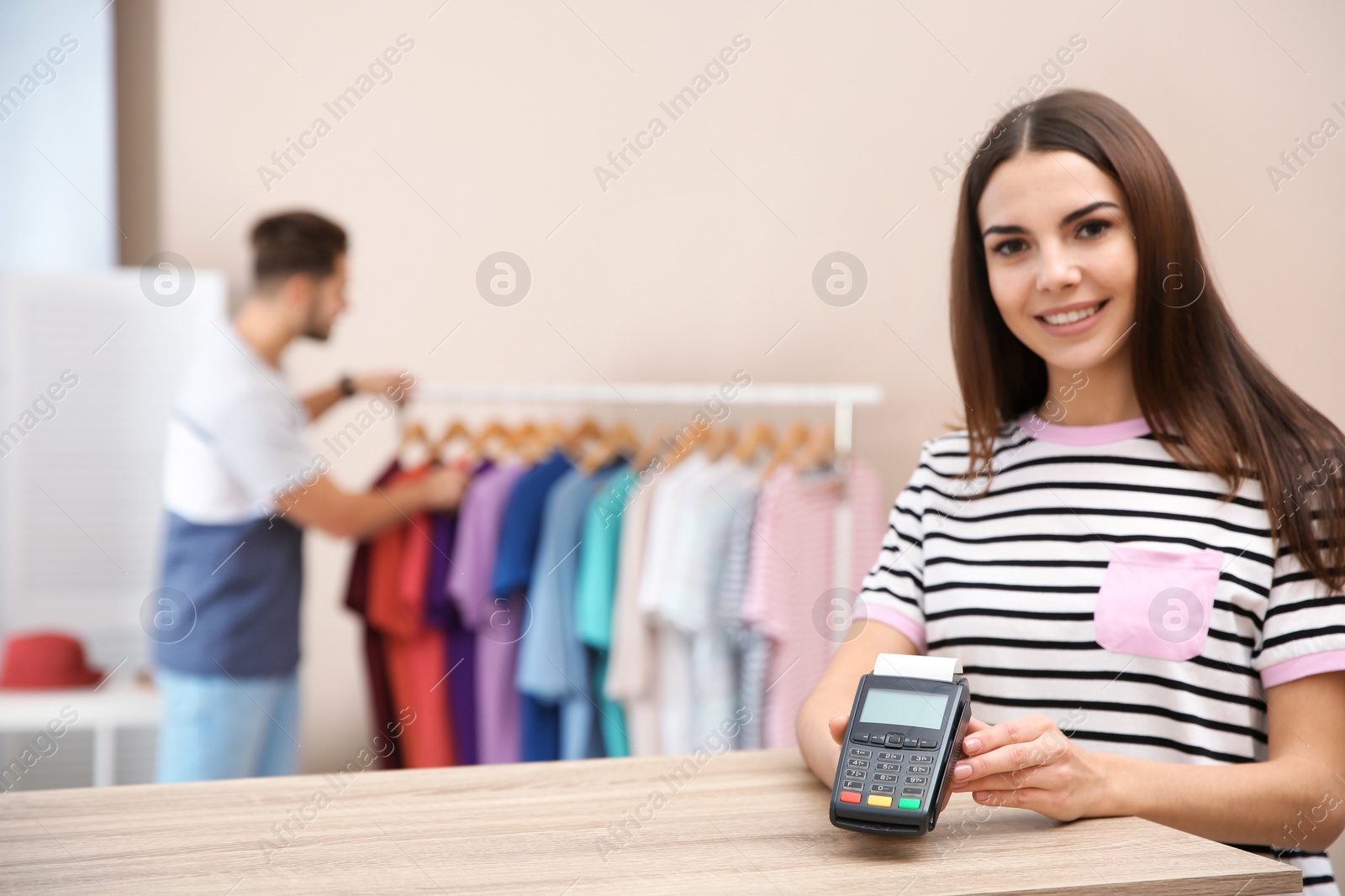 Photo of Female shop assistant with payment terminal at counter. Space for text