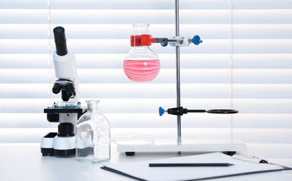 Photo of Laboratory analysis. Flask with pink liquid and microscope on white table