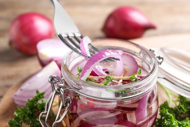Photo of Fork with slices of pickled onion over jar on table, closeup