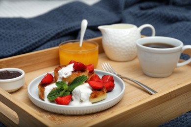 Photo of Delicious cottage cheese pancakes with fresh strawberries, sour cream and mint served on wooden tray, closeup