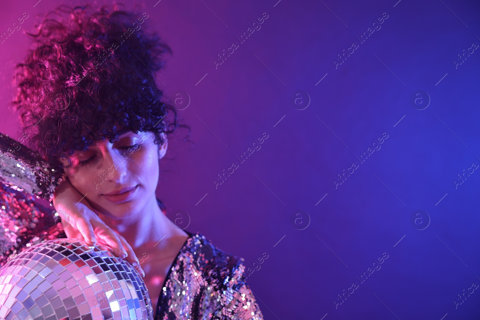 Photo of Beautiful young woman with disco ball posing on color background in neon lights. Space for text