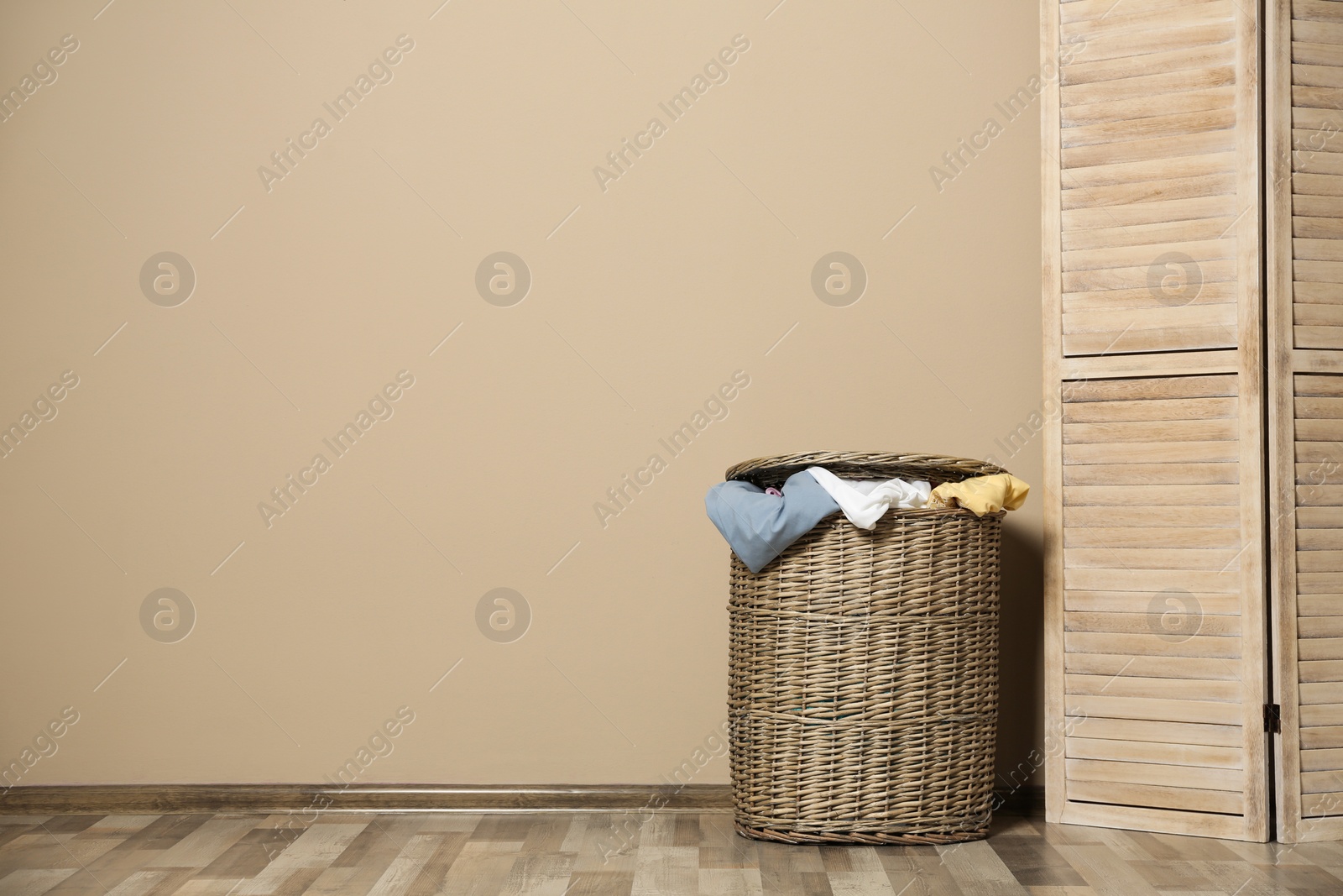 Photo of Wicker laundry basket full of dirty clothes on floor near wall. Space for text