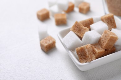 Photo of Different sugar cubes in bowl on white table, closeup. Space for text