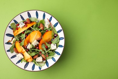 Tasty salad with persimmon, blue cheese, pomegranate and almonds served on light green background, top view. Space for text