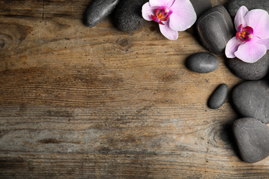 Stones with orchid flowers and space for text on wooden background, flat lay. Zen lifestyle